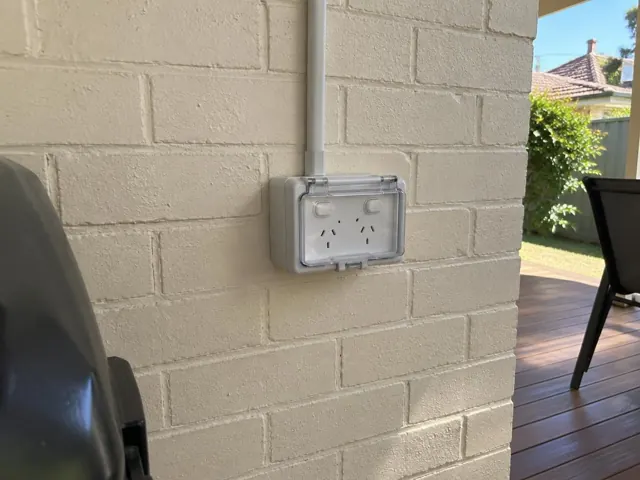 Outdoor double power point on a painted brick exterior wall beside a deck in Lambton